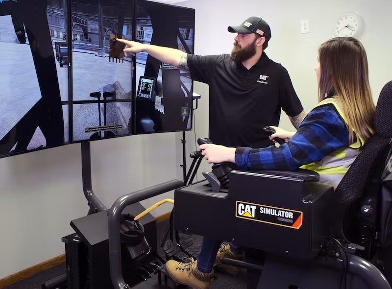 A Simformotion trainer explains how to operate an excavator effectively to a student training on a Cat Simulators system.